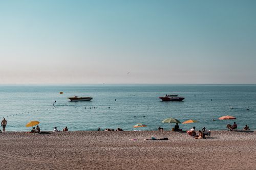 Free A tranquil beach scene with umbrellas, people relaxing, and boats on calm sea. Stock Photo
