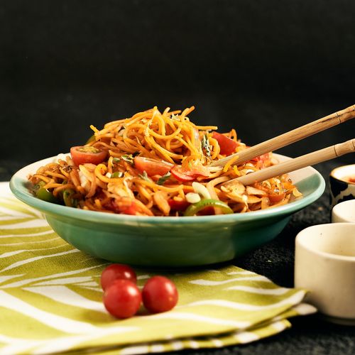 Free Tasty noodle dish garnished with fresh tomatoes in a green bowl, enhanced by dramatic lighting and a modern vibe. Stock Photo