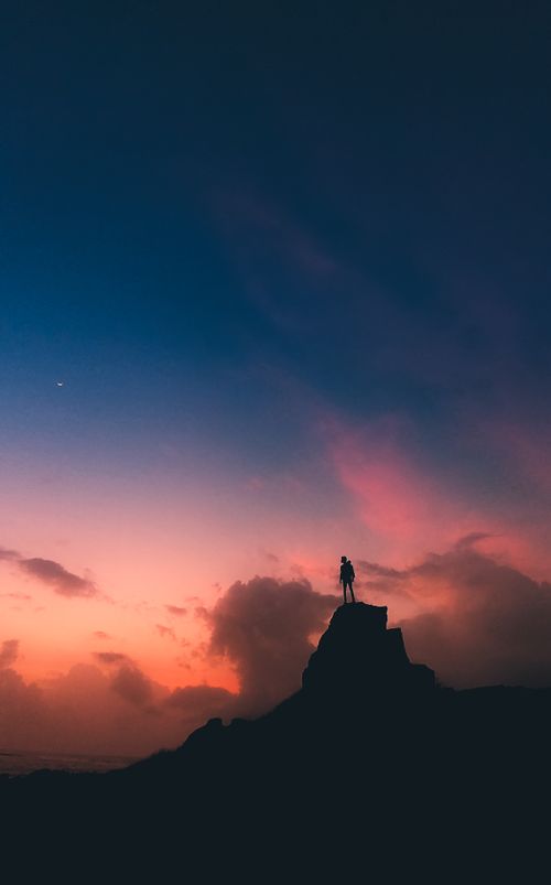 Free Hiker silhouetted against a stunning twilight sky atop a mountain peak, capturing the essence of adventure. Stock Photo