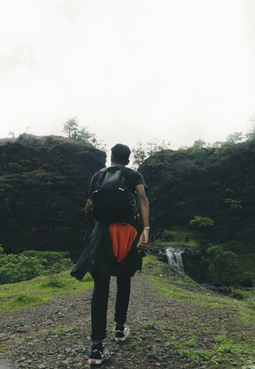 Free Hiker with backpack walking towards a waterfall in a lush green mountain area. Stock Photo