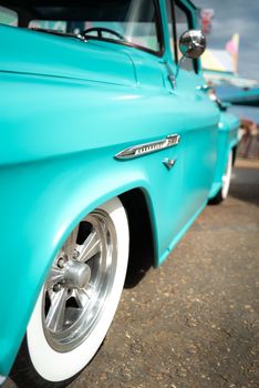 Close-up of a turquoise vintage car with white-wall tires on a street.