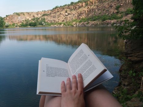 A peaceful moment reading by a serene lake with scenic cliffs in Ukraine.