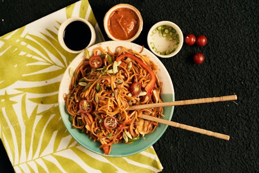 A vibrant bowl of noodles with fresh vegetables and accompanying sauces, perfect for food photography.