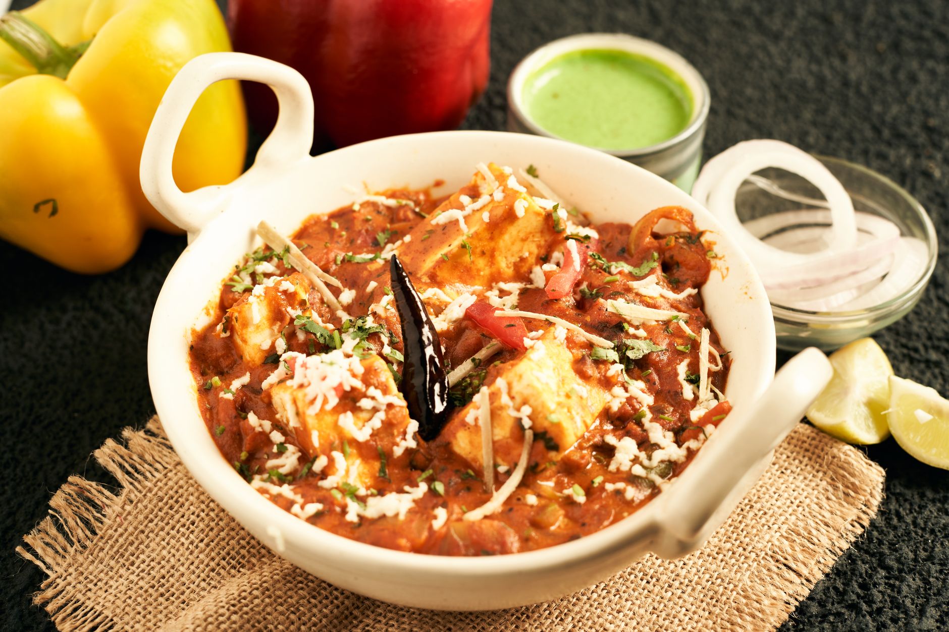 A generous bowl of kadai paneer showing golden-brown paneer cubes nestled among colorful bell pepper strips and green chilies in a rich, rustic tomato sauce, finished with fresh cilantro