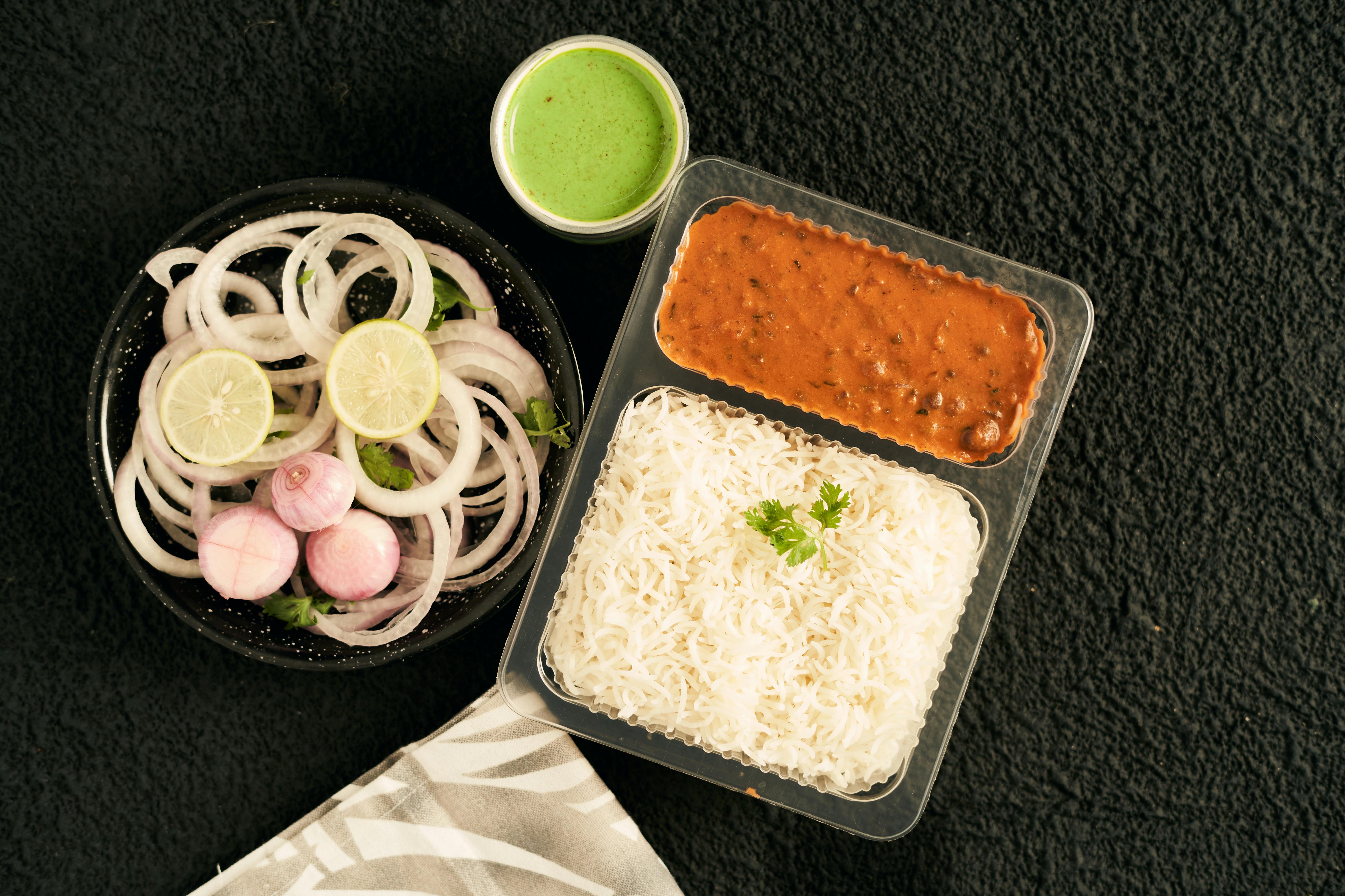 A vibrant Indian takeaway meal with rice, lentils, and fresh onions, perfect for lunch.