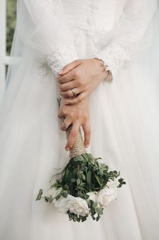 Close-up of a bride in a white dress holding a rustic bouquet, showcasing elegance and romance.