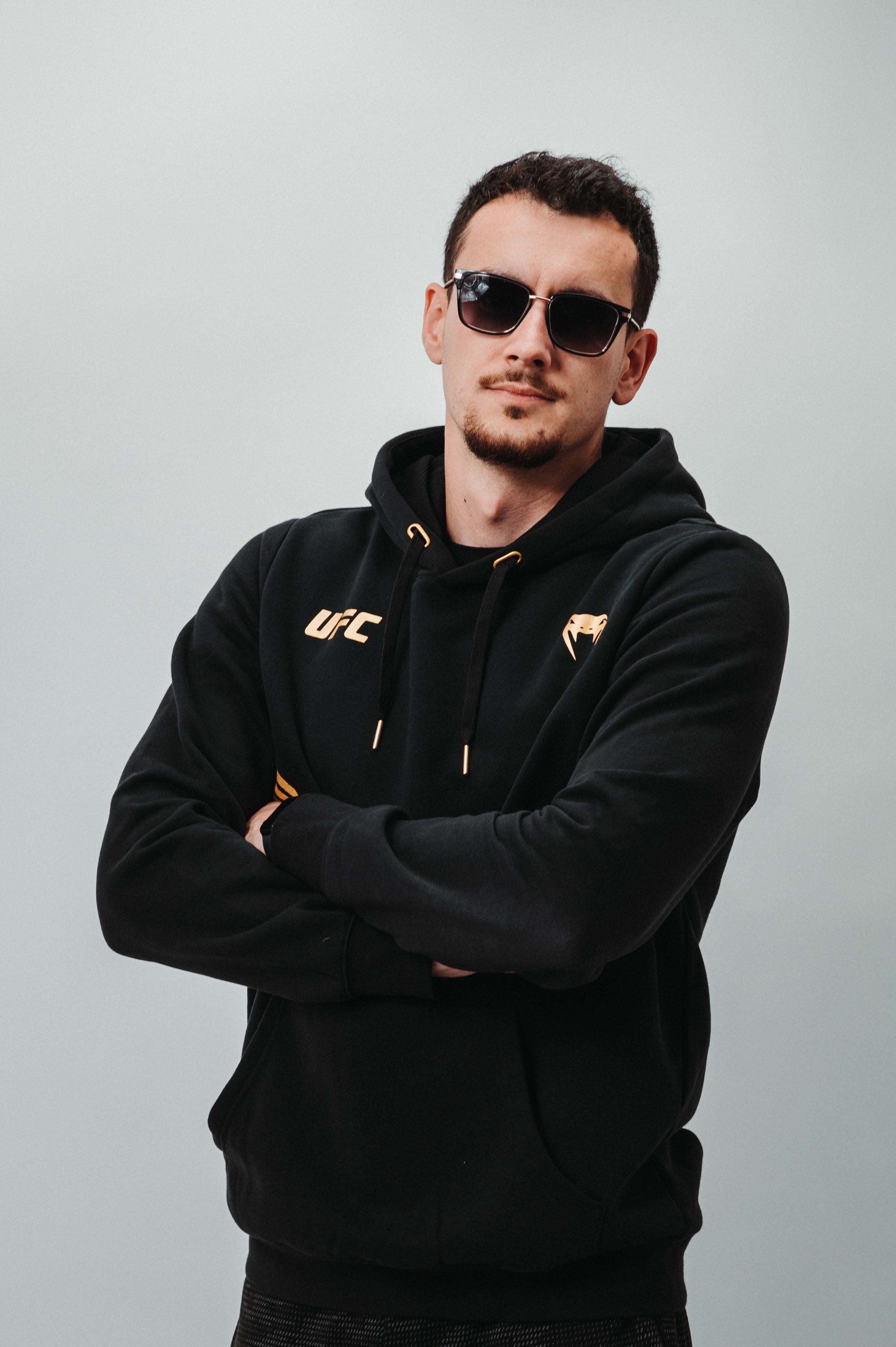 Portrait of a confident man wearing sunglasses and a black hoodie, posing with crossed arms.