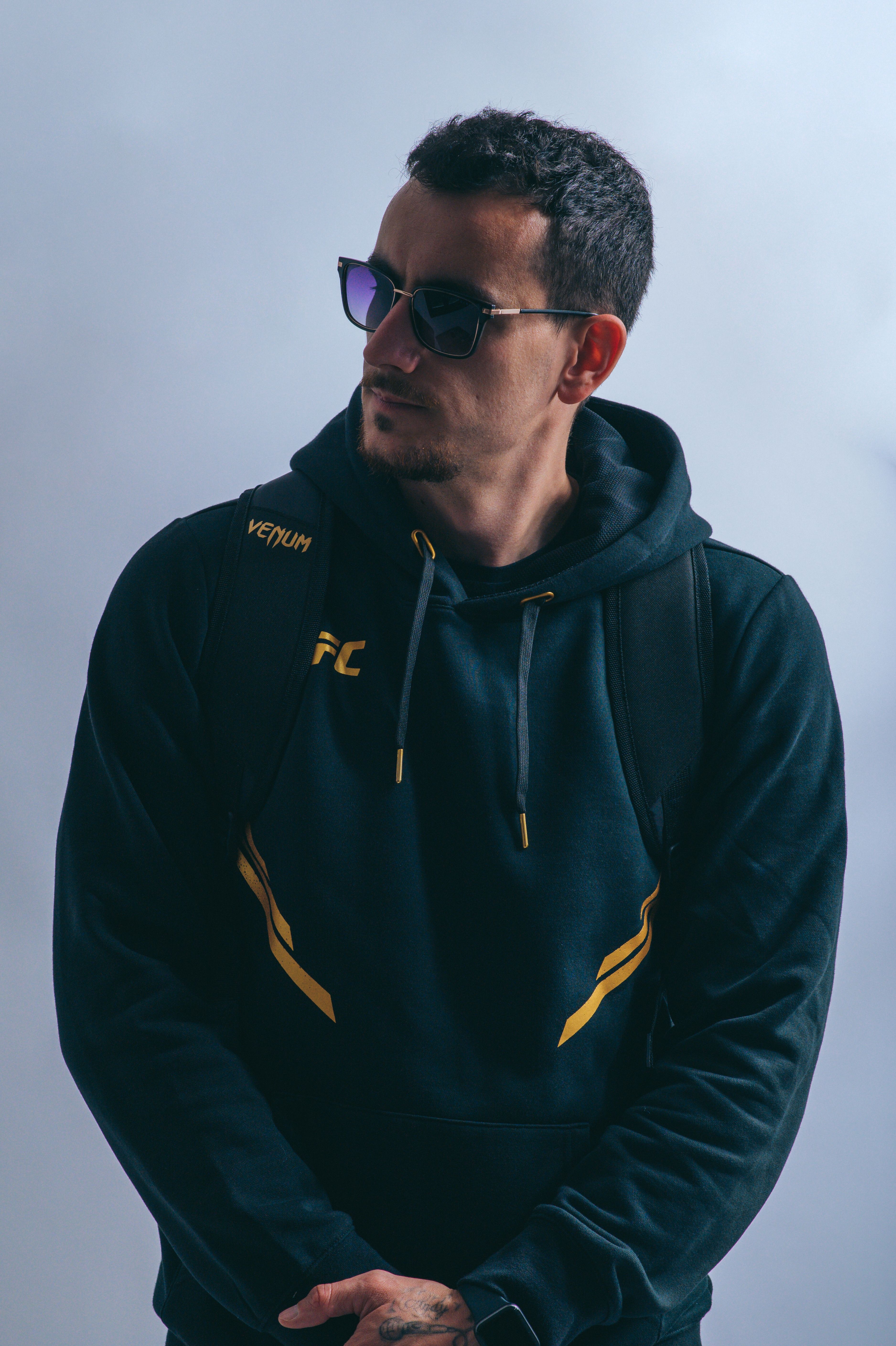 Portrait of a man in a black hoodie wearing sunglasses with a serious expression.
