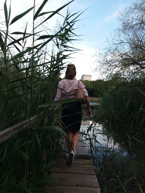 Back View of a Woman Walking on Wooden Walkway