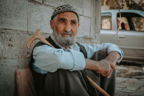 Free Portrait of a senior man sitting outdoors with a walking stick, exuding wisdom and resilience. Stock Photo