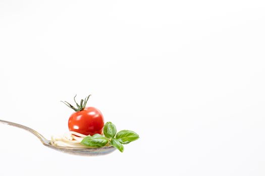 A cherry tomato and basil leaves beautifully presented on a spoon against a white background.