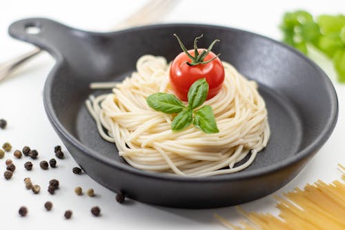 Cooked Spaghetti Pasta, a Whole Tomato and Leaves of Basil on a Pan 