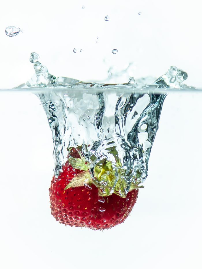 A vibrant strawberry making a splash in clear water on a white background