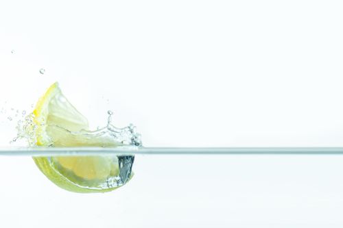 Free A vibrant lemon slice splashes into clear water, creating lively droplets on a white background. Stock Photo