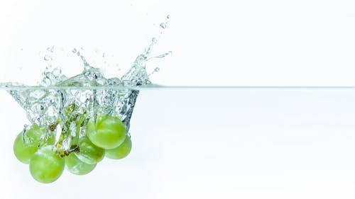 Close-up of Green Grapes Falling into Clear Water 
