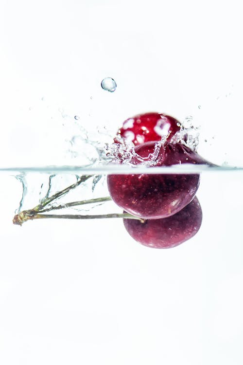 Close Up Photo of Ripe Cherries Dropped in Water Making a Splash