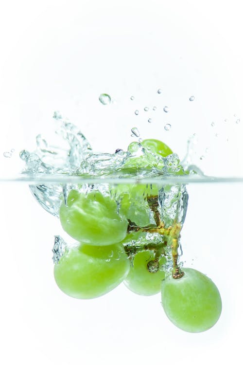 Close-up of Green Grapes Falling into Clear Water 