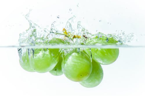 Close-up of Green Grapes Falling into Clear Water 