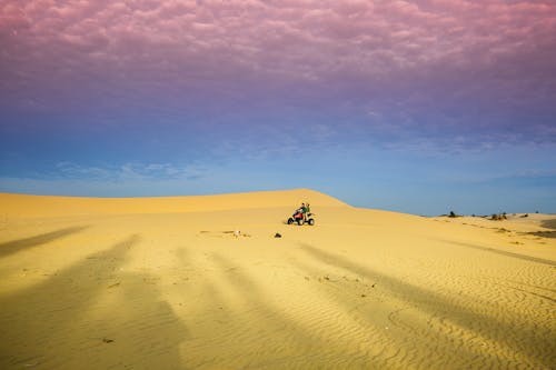 People Riding Quad Bike on Desert Under Blue Sky