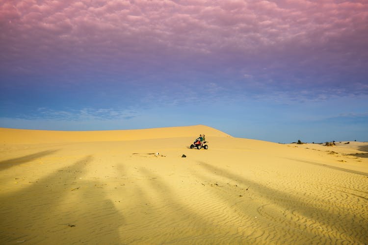 People Riding Quad Bike On Desert Under Blue Sky