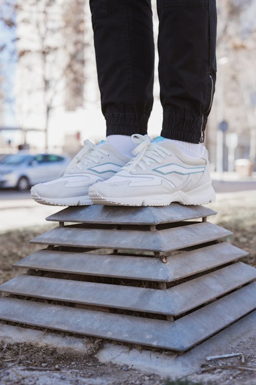 A Person in Black Pants Wearing White Sneakers Standing on a Metal Platform