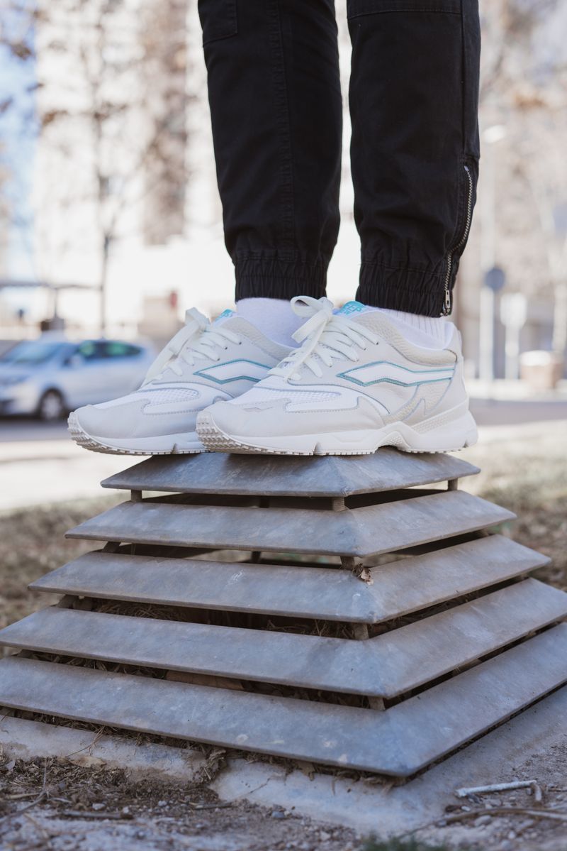 Persona calzando zapatillas blancas de pie sobre una plataforma metálica
