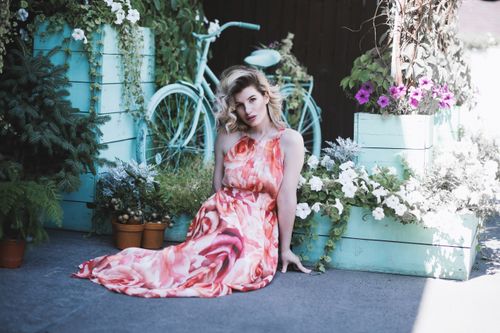 Free A stylish woman in a floral dress sits surrounded by plants and a vintage bicycle. Stock Photo