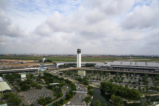 Aerial view of a bustling airport with control tower and surrounding landscape, highlighting infrastructure.