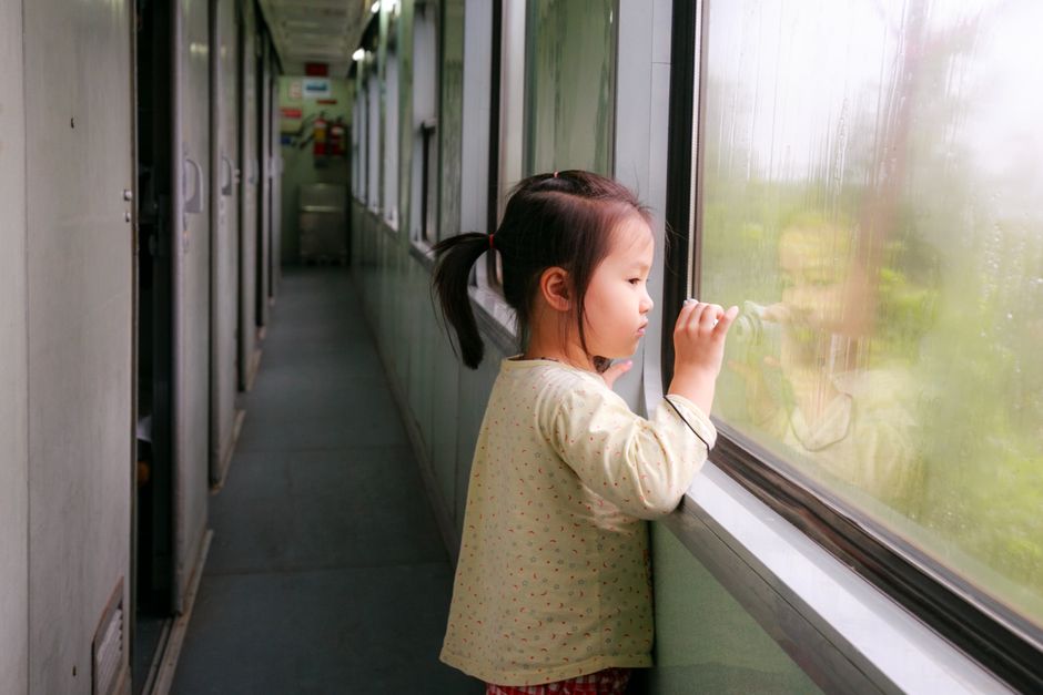 Young girl gazes out of a train window, capturing a moment of reflection during travel.