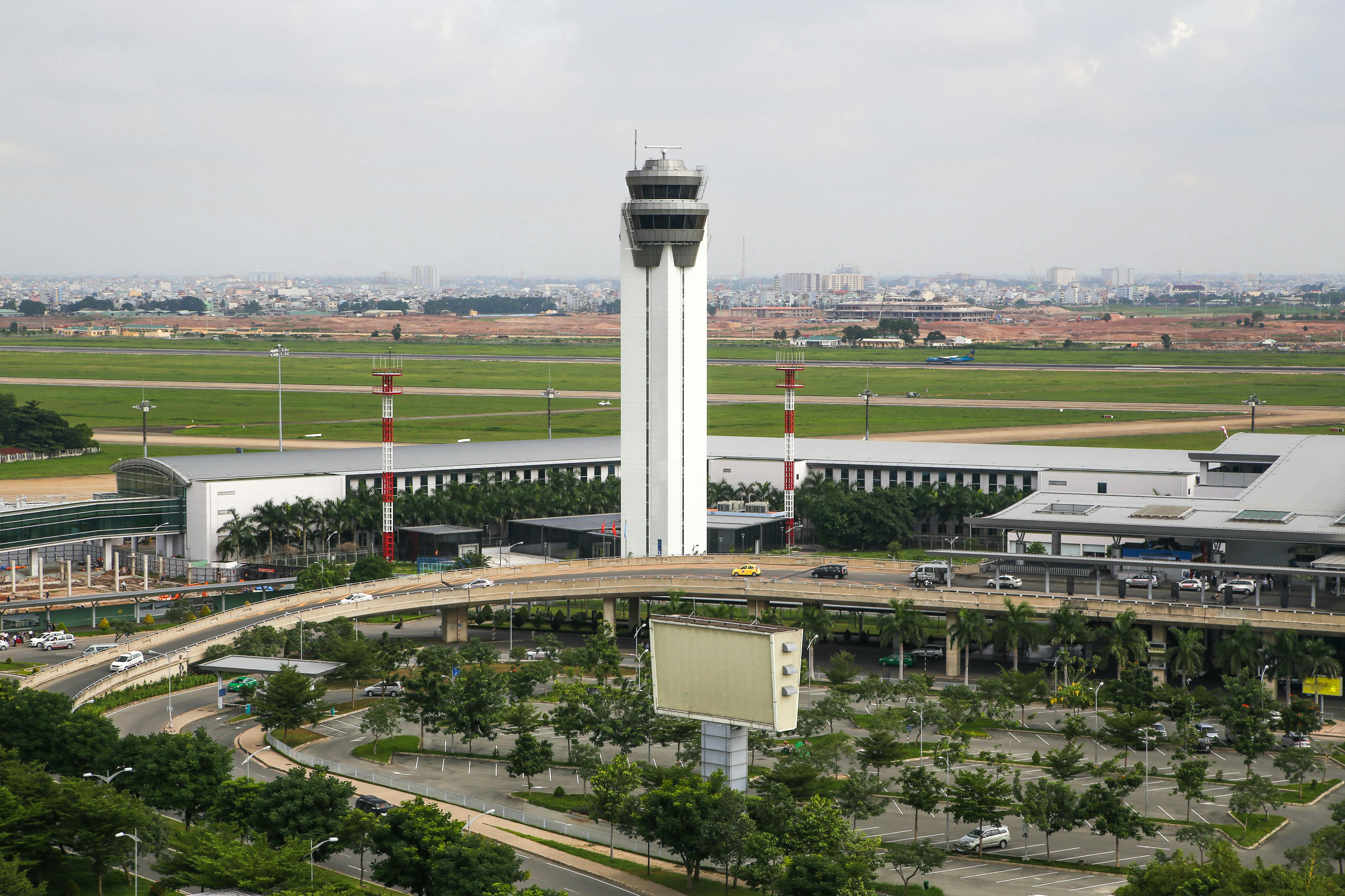 Aerial view of a busy airport with a prominent control tower, surrounded by roads and greenery.