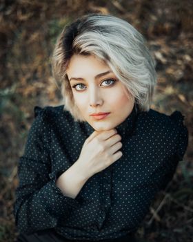 Striking portrait of a woman with short blonde hair posing outdoors in a thoughtful manner.