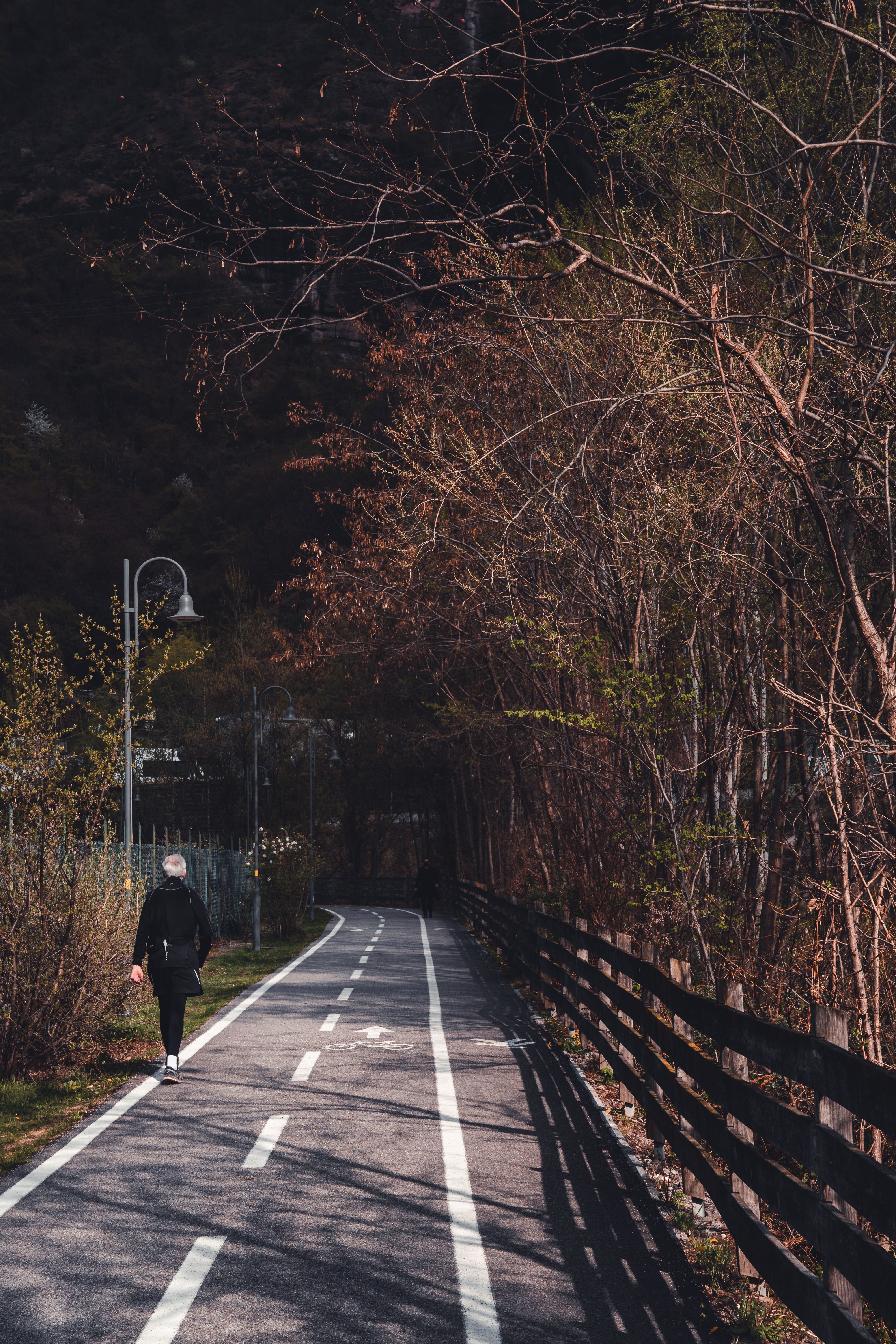 A Woman in Black Jacket Walking on Gray Concrete Pathway · Free Stock Photo
