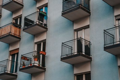 Free Side view of a modern apartment building with multiple balconies featuring plants and glass windows. Stock Photo