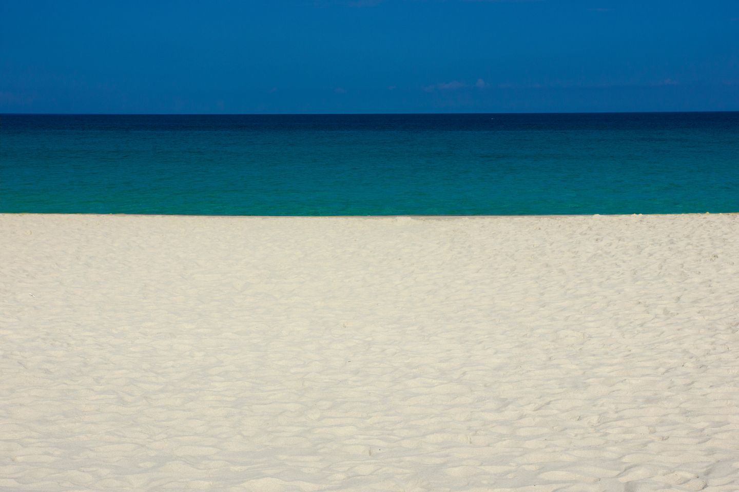 An empty stretch of white sand and open ocean under a clear Hawaiian sky