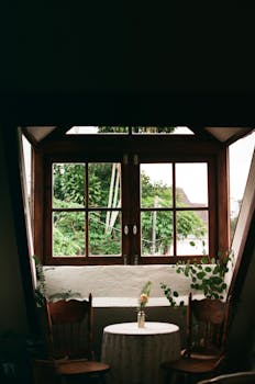 Warm interior with wooden windows framing lush greenery outside, creating a serene atmosphere.