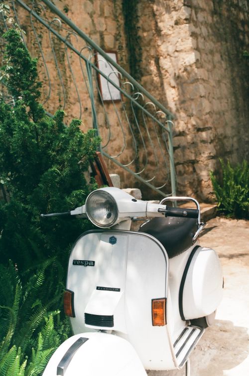 Free A vintage white Vespa motor scooter parked by a stone wall with greenery. Stock Photo