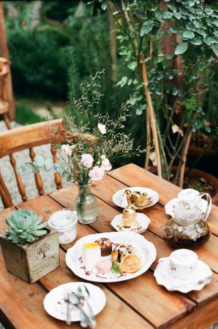 Charming outdoor tea setup with desserts, floral arrangement, and rustic decor.