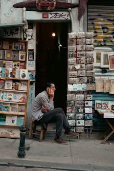Man seated by a busy urban bookstore talking on the phone, capturing street life.