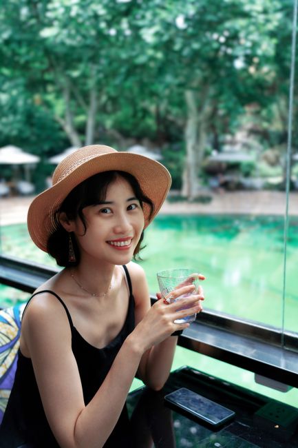 Smiling woman in a hat enjoying a refreshing drink by the pool during summer.