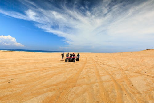 People Standing Beside a Quad Bike on Brown Sand Under Blue Sky
