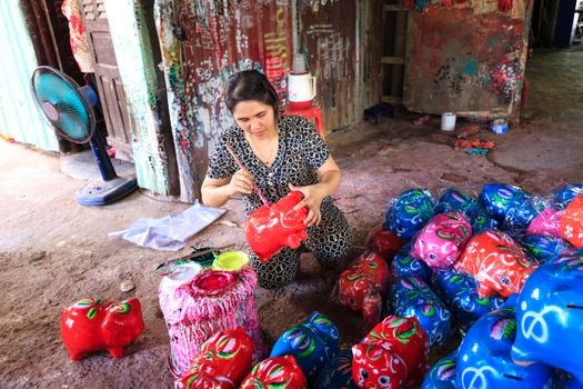 A woman carefully paints vibrant piggy banks in an artistic workshop.