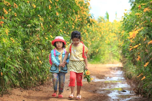 Kids Walking on a Pathway Between Green Plants