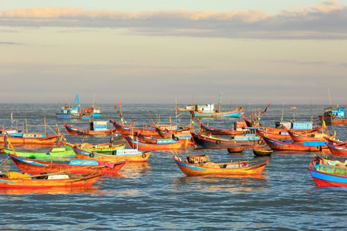 Free Vibrant fishing boats float on a calm sea during sunset, creating a picturesque seascape. Stock Photo