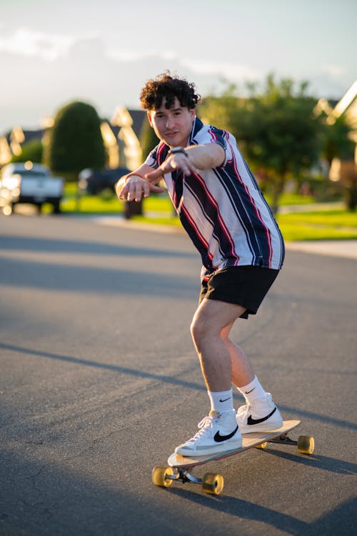 A Man in Striped Shirt Riding on a Skateboard while Posinga the Camera