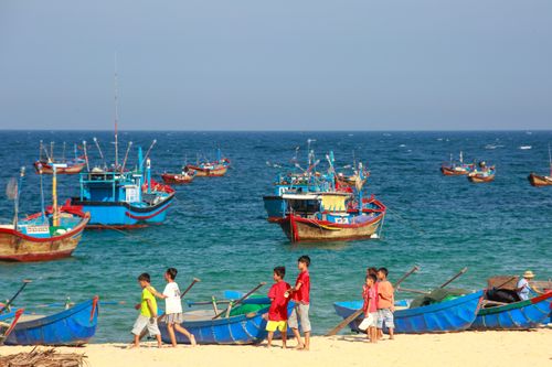 Free Children playing by colorful fishing boats on a sunny beach with clear blue sea. Stock Photo