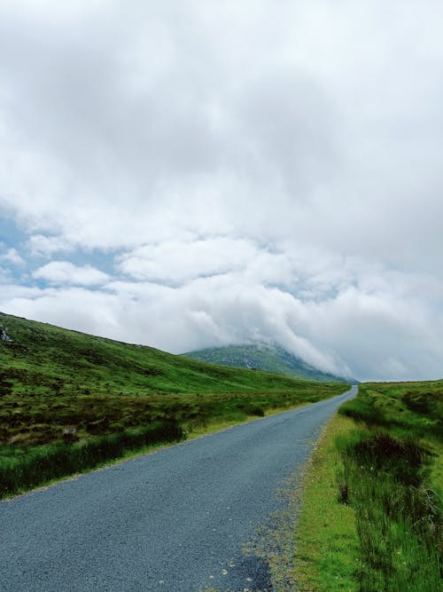 Gray Asphalt Road Between Green Grass Field Under Cloudy Sky