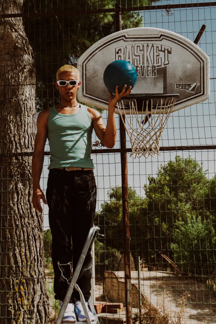 Young Man Posing On Top Of A Ladder With A Basketball In Hand