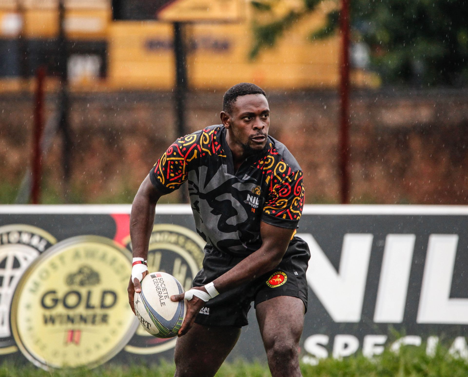 Rugby player in colorful jersey holding ball during a rainy match outdoors.