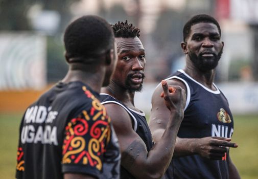Three male athletes discussing strategy during a sports event in Uganda.