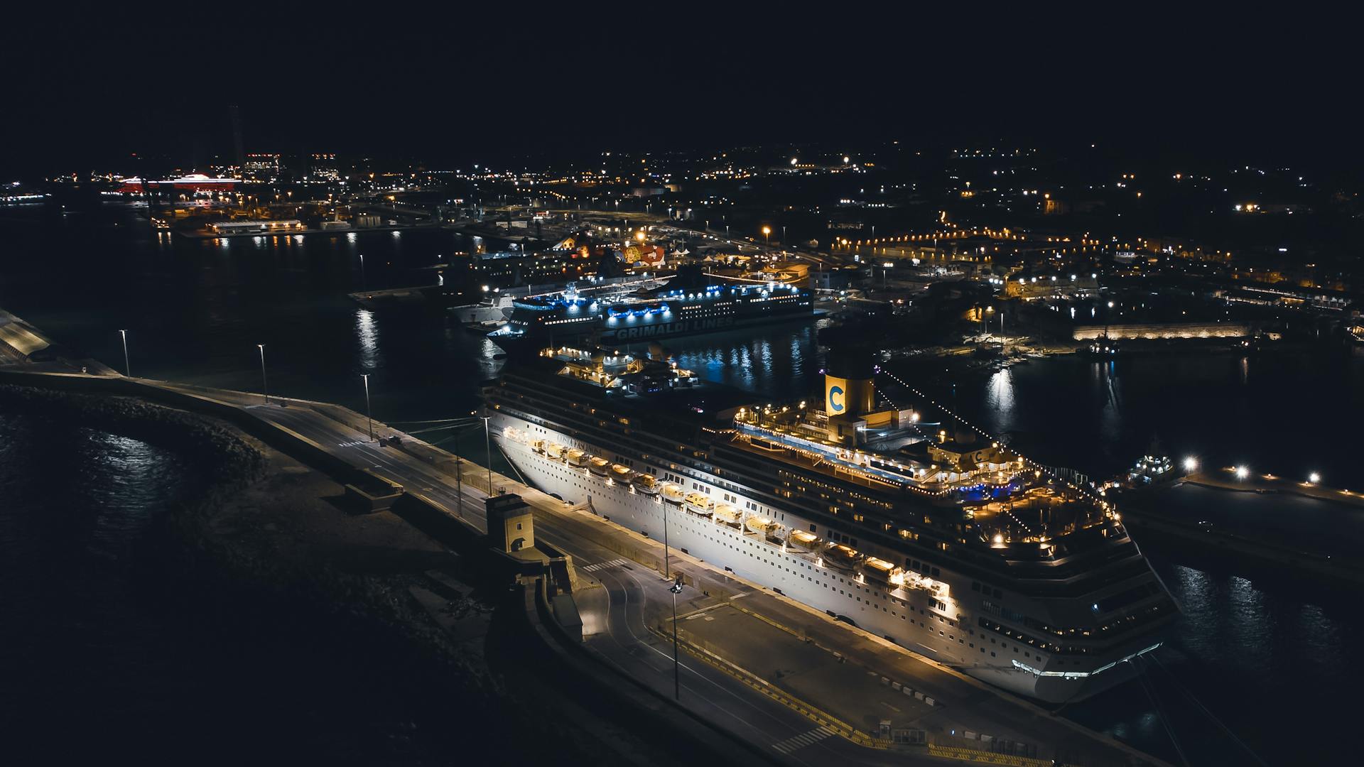 Stunning aerial view of a brightly illuminated cruise ship docked in a bustling harbor at night.